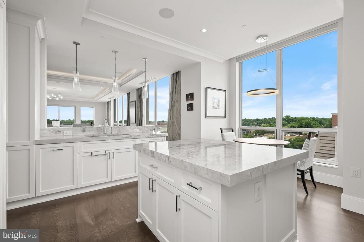 A view of a sparkling white and gray kitchen/dining area with sleek white cabinetry and shiny patterned countertops